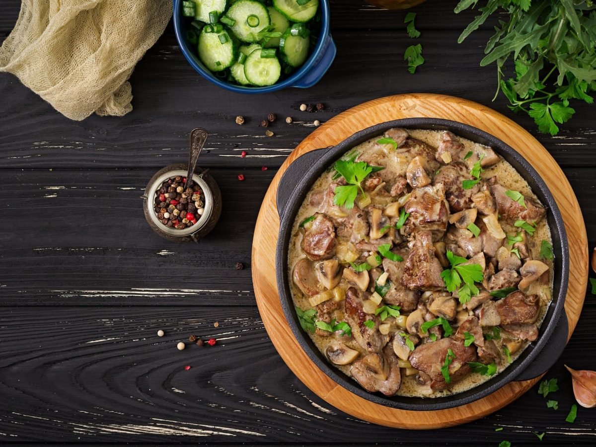 Boeuf Stroganoff auf schwarzem Holz. Kräuter und Stofftuch auf dem Tisch. Aufnahme aus der Vogelperspektive.