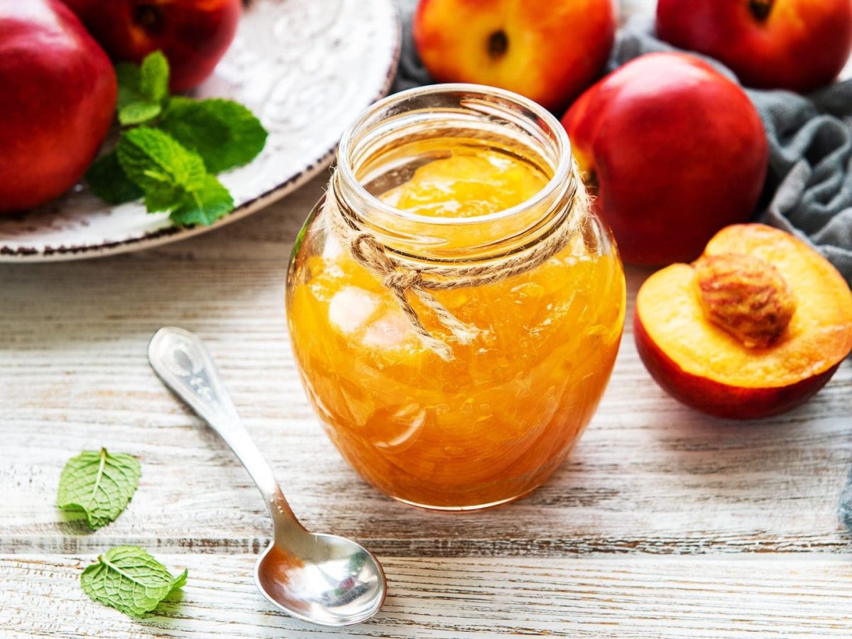 Glas Nektarinen-Marmelade mit Schuss, daneben Löffel und Nektarinen