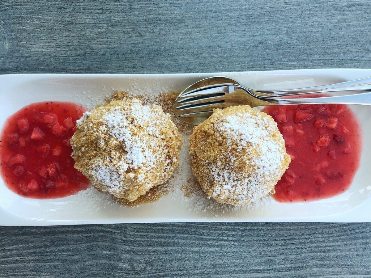 Zwei Topfenknödel mit Erdbeer-Rhabarber-Kompott auf einem länglich-weißen Teller mit Besteck