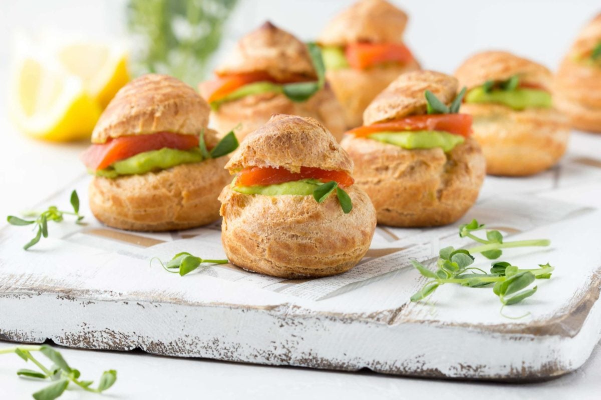 Windbeutel mit Lachs und Erbsencreme gefüllt, serviert auf einem grauen Brett mit frischer Kresse