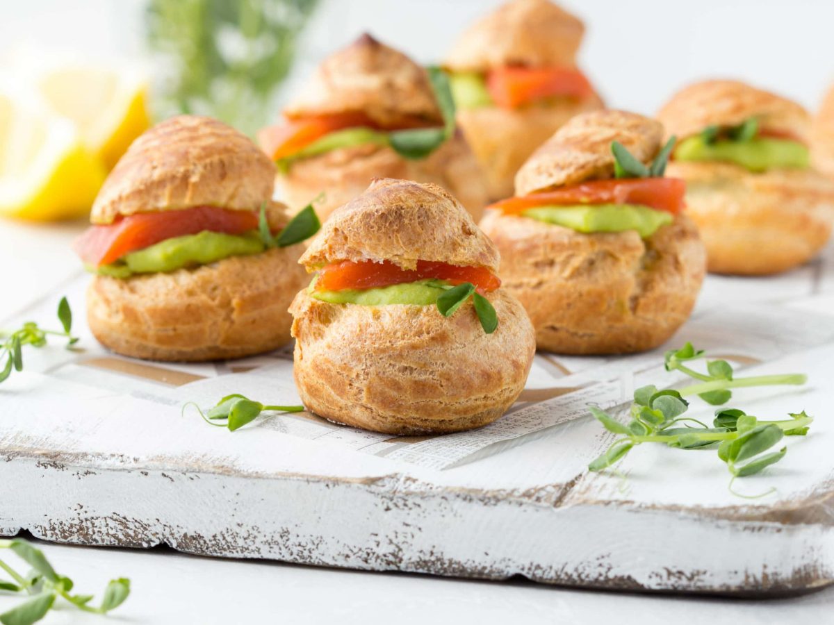 Windbeutel mit Lachs und Erbsencreme gefüllt, serviert auf einem grauen Brett mit frischer Kresse