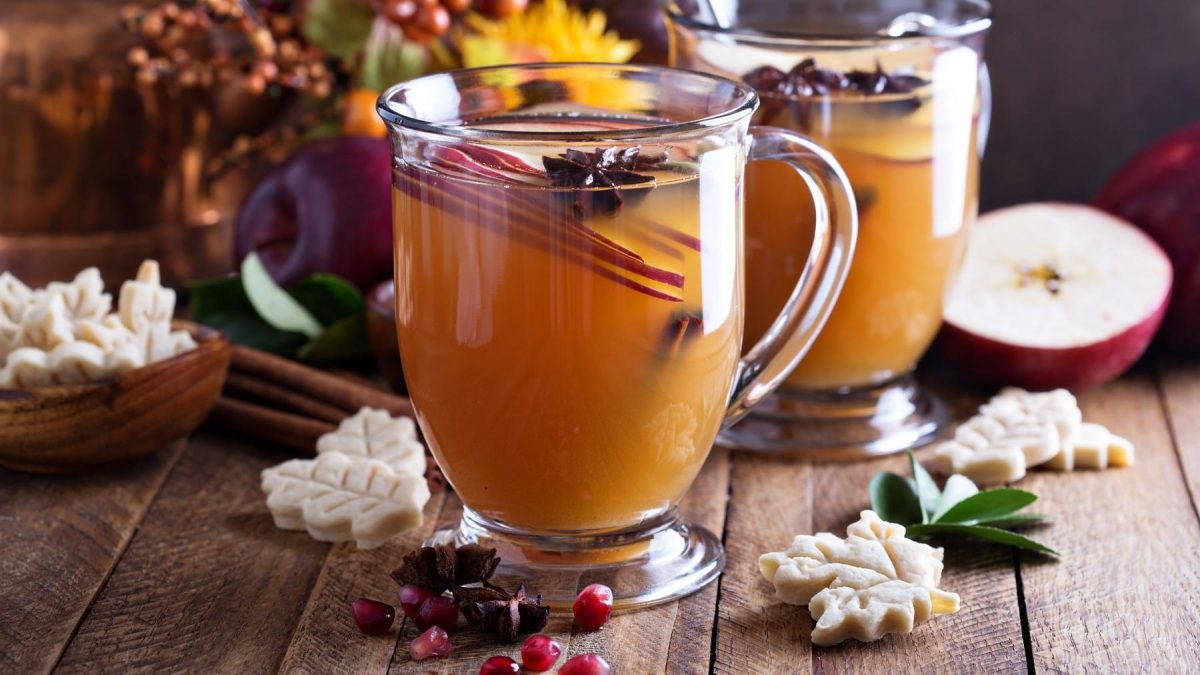 Apfel-Grog mit Sternanis und Apfelscheiben, serviert in kleinen, gläsernen Tassen auf einem weihnachtlich gedeckten Holztisch.