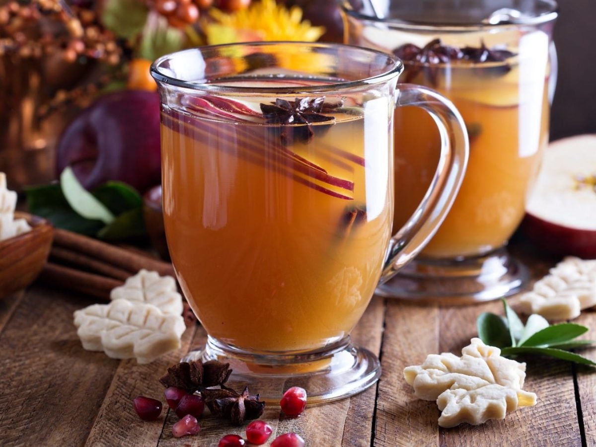 Apfel-Grog mit Sternanis und Apfelscheiben, serviert in kleinen, gläsernen Tassen auf einem weihnachtlich gedeckten Holztisch.