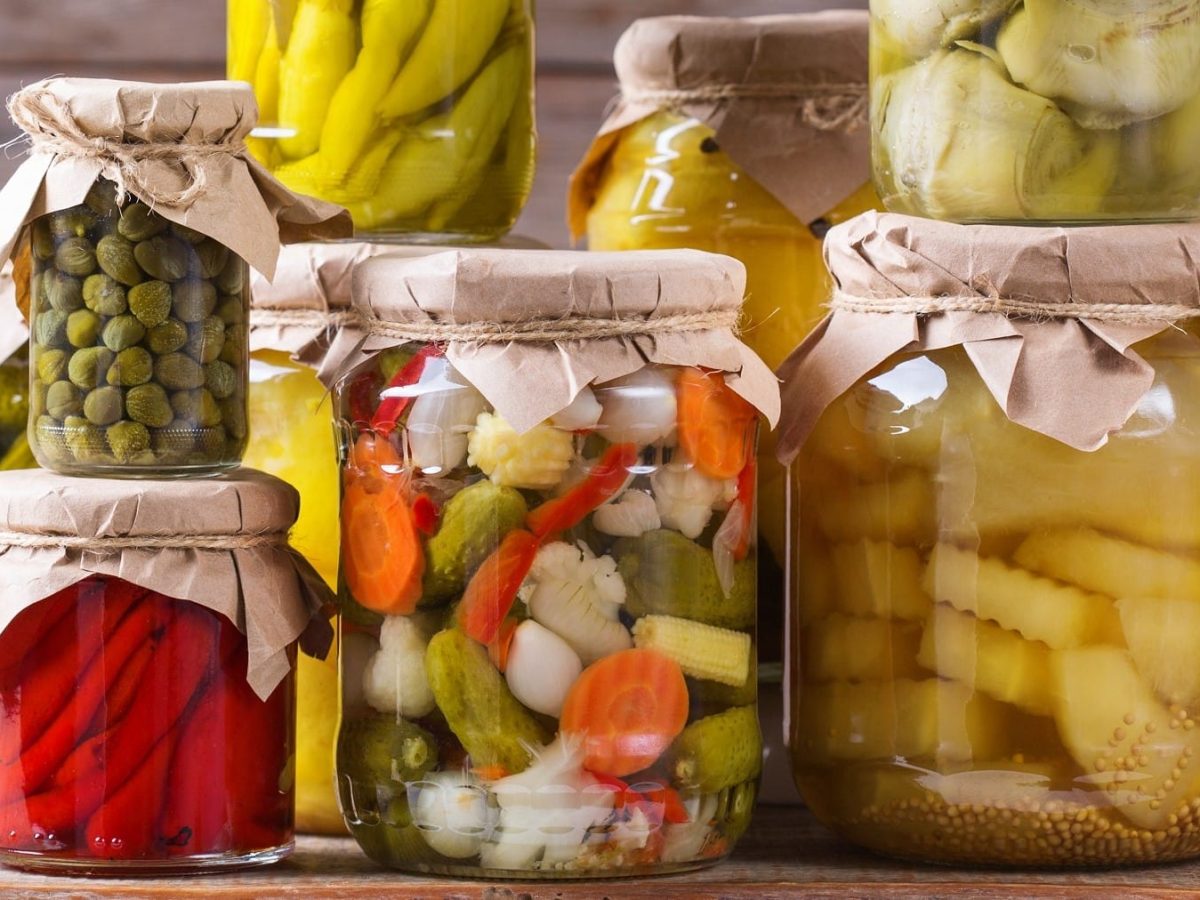 Mixed Pickles, gemischtes eingelegtes Gemüse in einem Einmachglas, umgeben von weiteren Gläsern mit eingemachtem Gemüse.