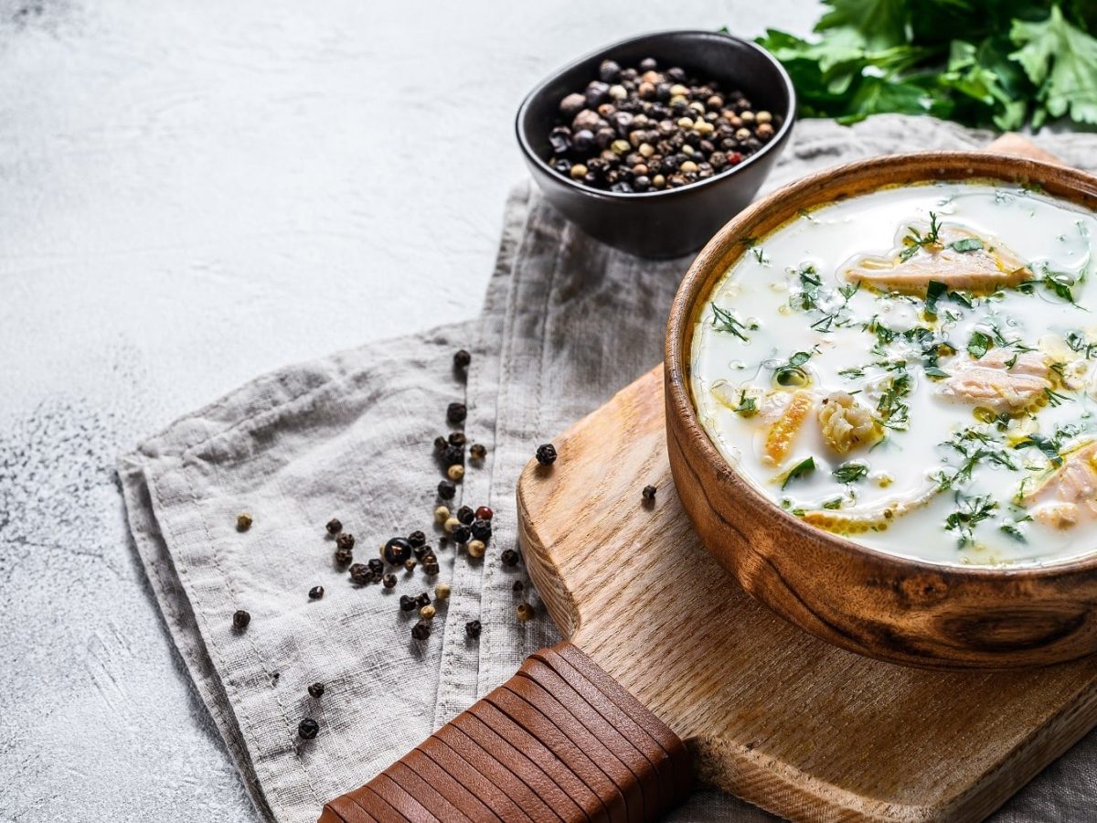 Norwegische Fischsuppe mit frischem Dill, cremiger Sahne und Wurzelgemüse, serviert in einer großen Schale auf einem rustikalen Holzbrett.