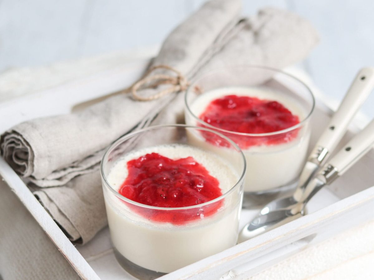 Panna Cotta mit selbst gemachter Erdbeersauce in zwei Gläsern auf weißem Tablett