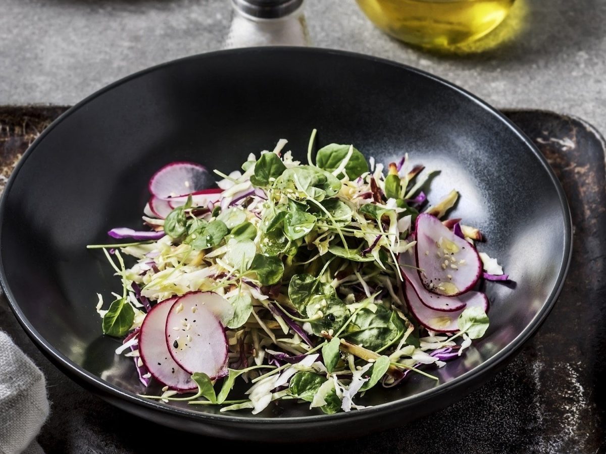 Knackiger Rohkostsalat, bestehend aus Rotkraut, Spitzkohl, Spinat und Radieschen, getoppt mit feiner Vinaigrette und Sesam