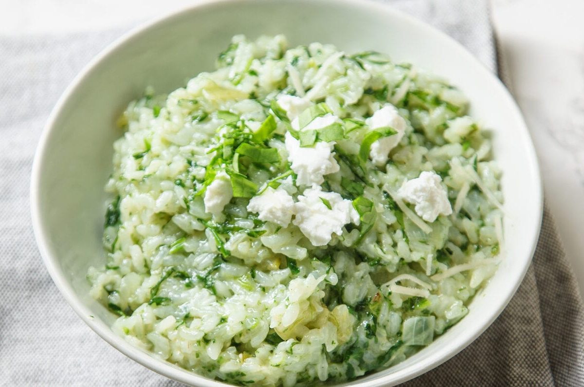 Spinat-Risotto mit Ziegenkäse auf weißem Teller vor marmoriertem Untergrund