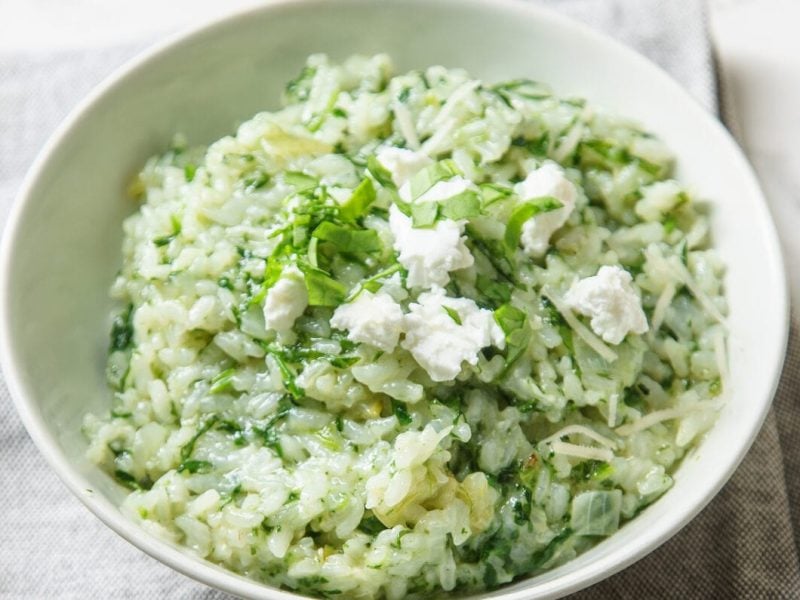 Spinat-Risotto mit Ziegenkäse auf weißem Teller vor marmoriertem Untergrund