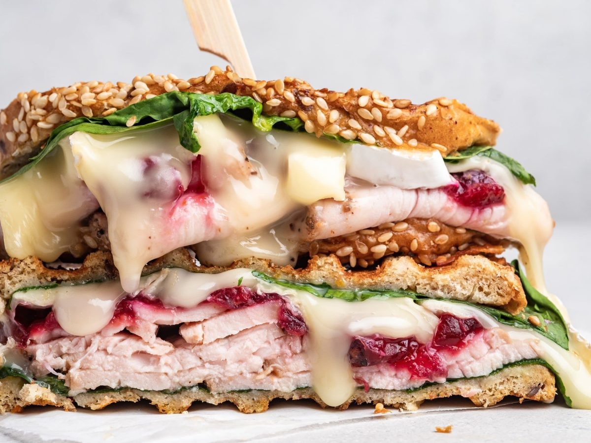 Saftiges Truthahn-Sandwich mit Cranberry-Sauce, Spinat, geschmolzenem Käse und Sesam auf einem weißen Teller