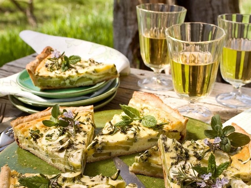 Zucchini-Quiche mit Pfefferminze und Weingläser auf einer Picknickdecke