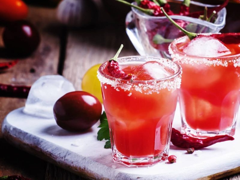 Zwei Gläser mit Chili-Kirsch-Mocktails stehen neben Kirschen und einer Schale voll Chilis