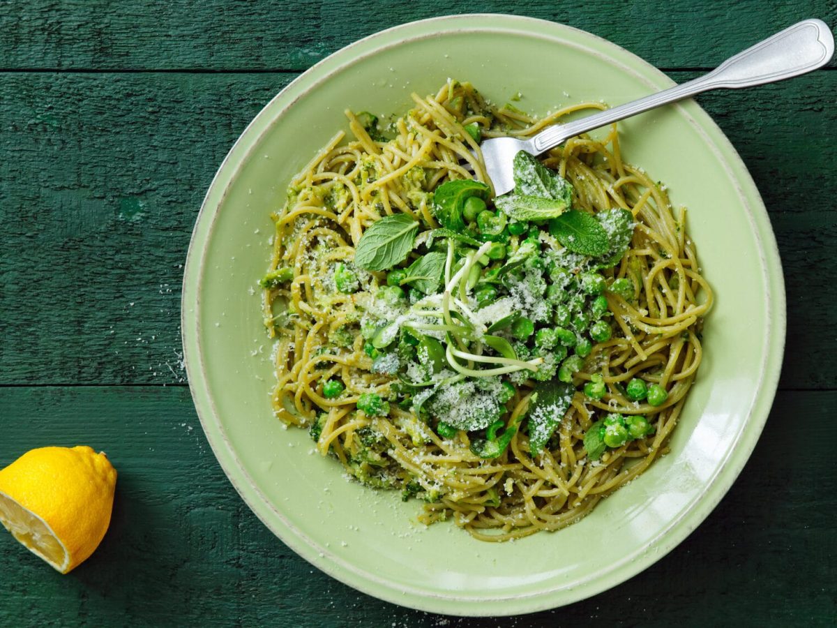 Frische Pasta-Bowl mit Erbsen und Minze auf weißem Teller vor grünem Untergrund