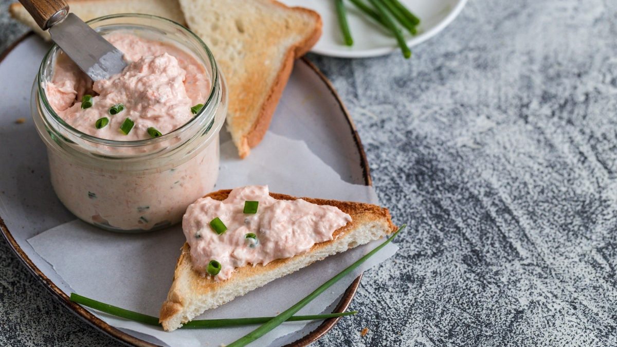 Lachscreme mit Toast, garniert mit frischem Schnittlauch und serviert auf einem Keramikteller auf Holz.