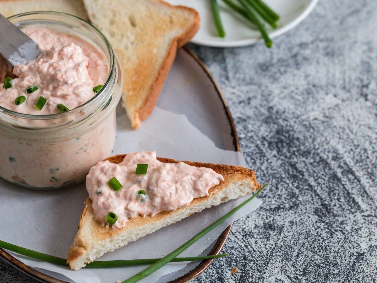 Lachscreme mit Toast, garniert mit frischem Schnittlauch und serviert auf einem Keramikteller auf Holz.