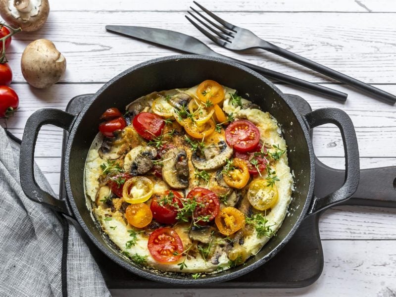 Würziges Omelette mit Tomate und Chili in schwarzer Pfanne vor hellem Untergrund