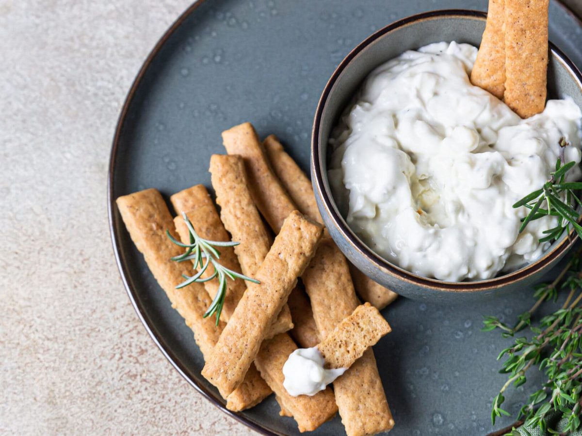 Schneller Birnen-Dip mit Gorgonzola in Schüssel auf blauem Teller, daneben Rosmarin und Brotsticks