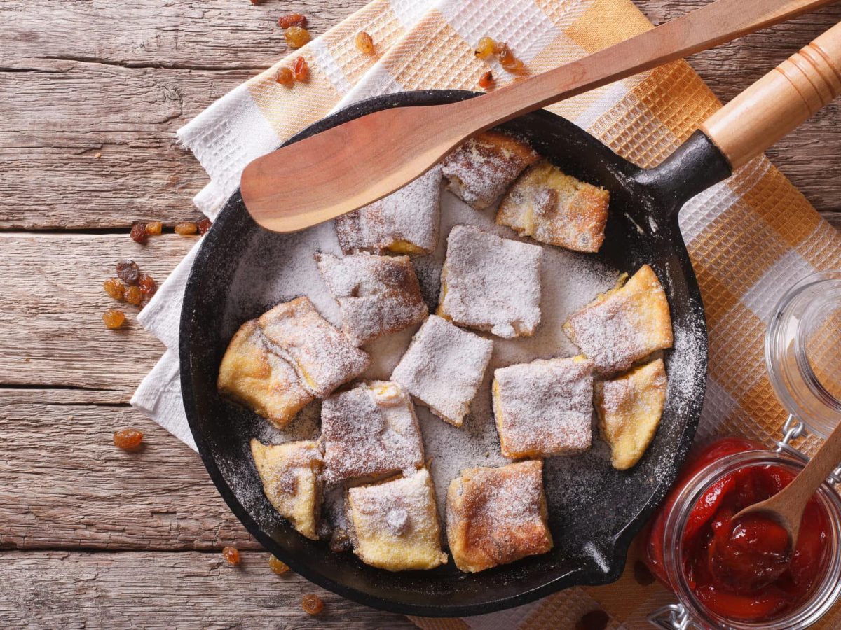 Kaiserschmarrn aus dem Ofen in Pfanne auf Holzuntergrund, daneben Zwetschgenkompott