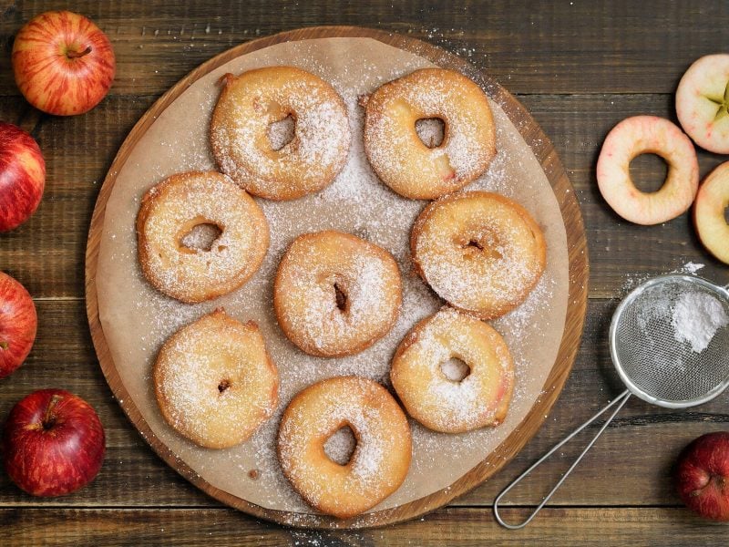 Selbst gemachte Apfelbeignets auf Teller, daneben Puderzucker