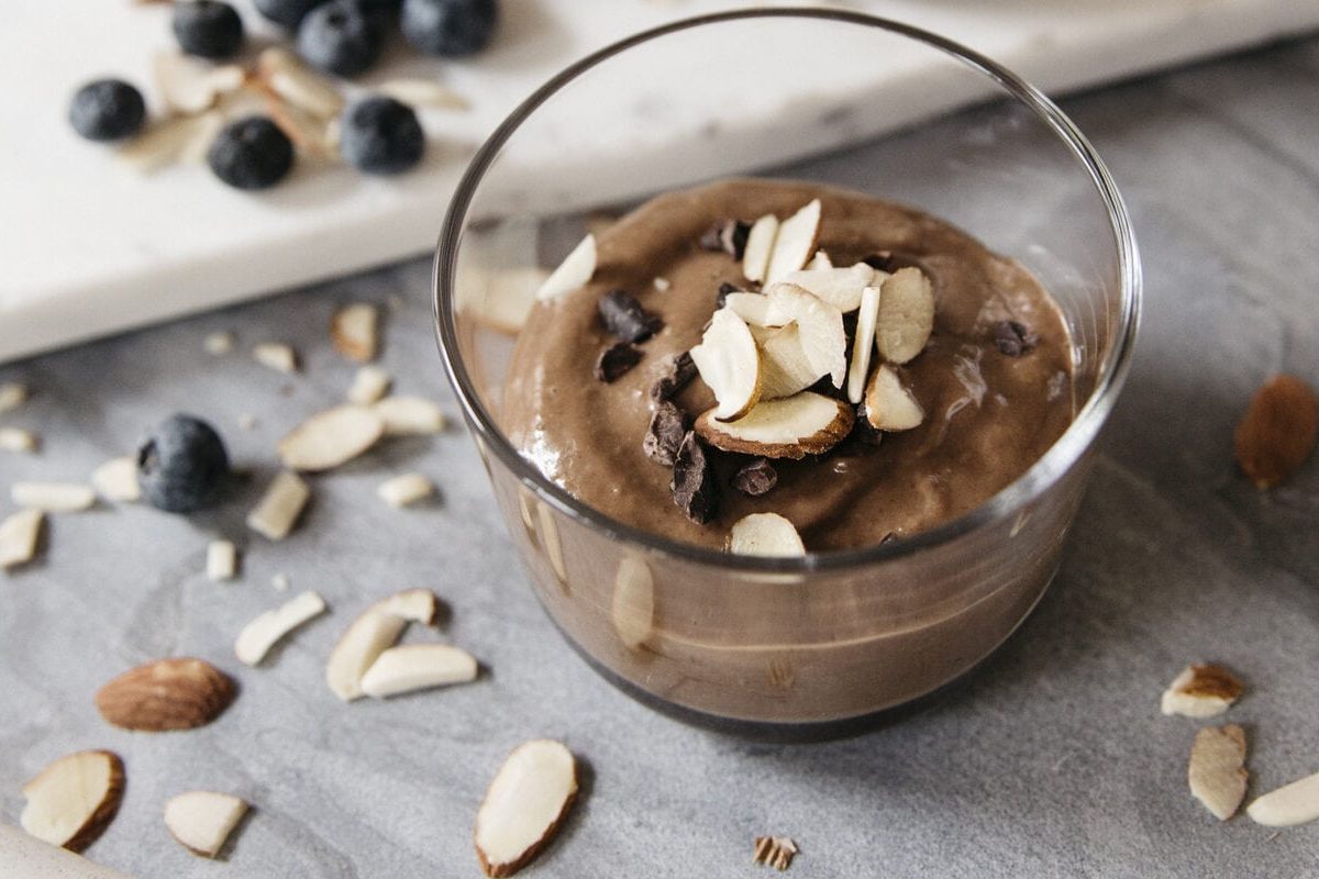 Schokoladiger Chia Pudding mit Mandeln in kleinem Glas, daneben Mandelsplitter