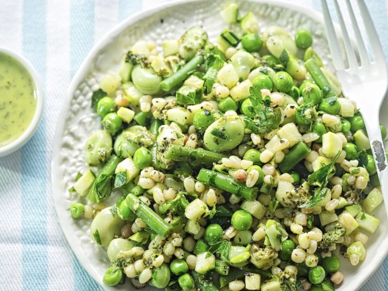 Grüner Salat mit Estragon-Dressing auf weißem Porzellan vor hellblau-weiß gestreiftem Hintergrund