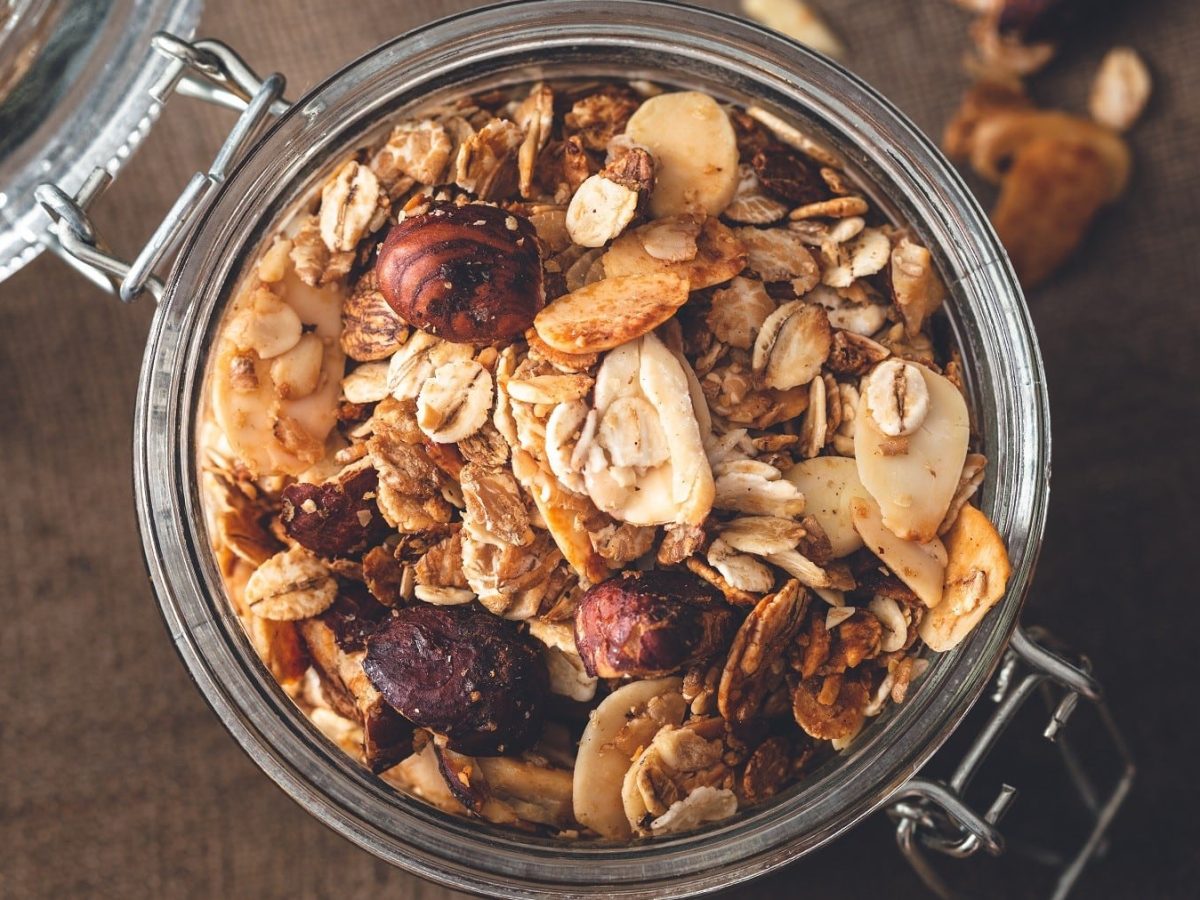 Geröstetes Müsli mit Haferflocken, Nüssen und Trockenfrüchten, serviert in einem Einweckglas auf einem Holztisch.