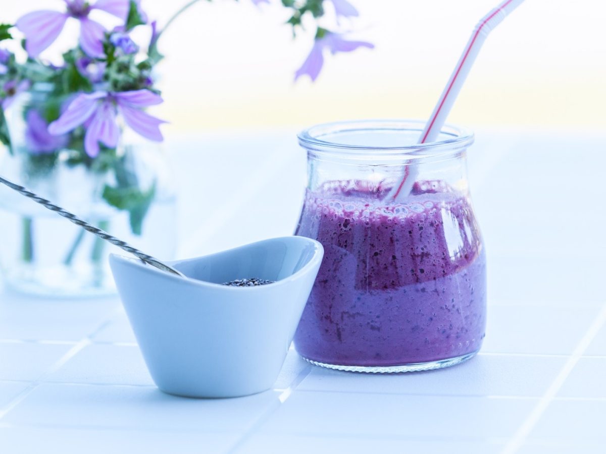 Brombeer-Smoothie mit Chia in hellem Ambiente neben lila Blüten.