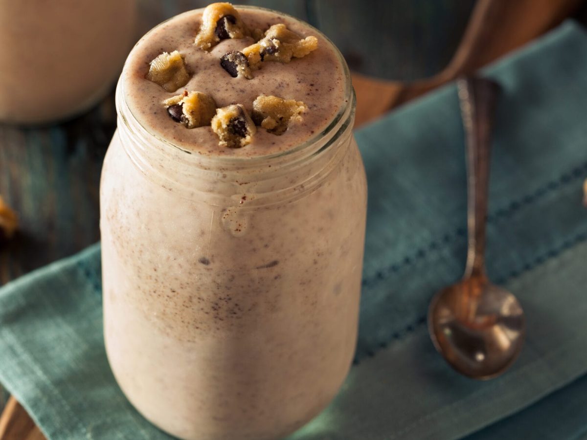 Veganer Cashew-Shake mit Schokolade in großem Glas, garniert mit Keksstücken