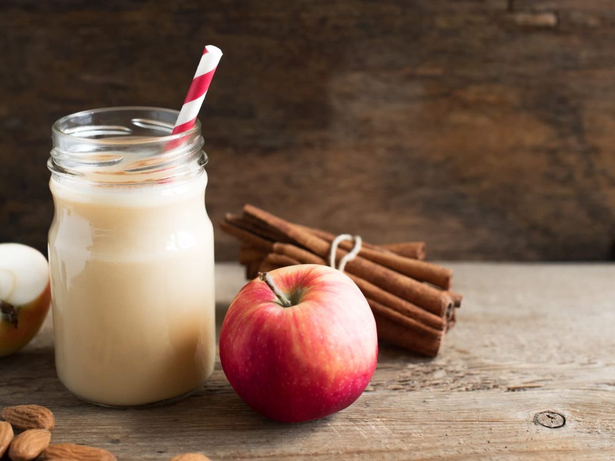 Power-Protein-Smoothie mit Apfel in Glas mit rotem Strohhalm, daneben Apfel und Zimtstangen