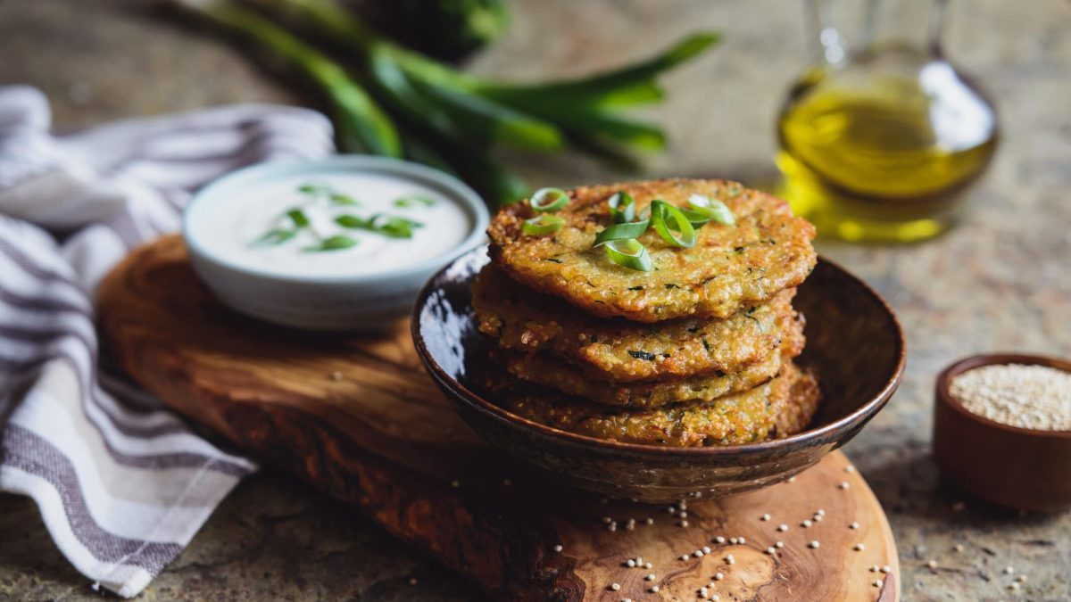 Pfiffige Quinoa-Bratlinge mit Joghurt-Dip in Teller auf Holz, dahinter Dip und Lauch