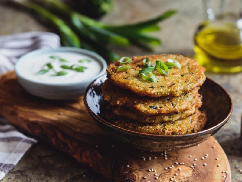 Pfiffige Quinoa-Bratlinge mit Joghurt-Dip in Teller auf Holz, dahinter Dip und Lauch