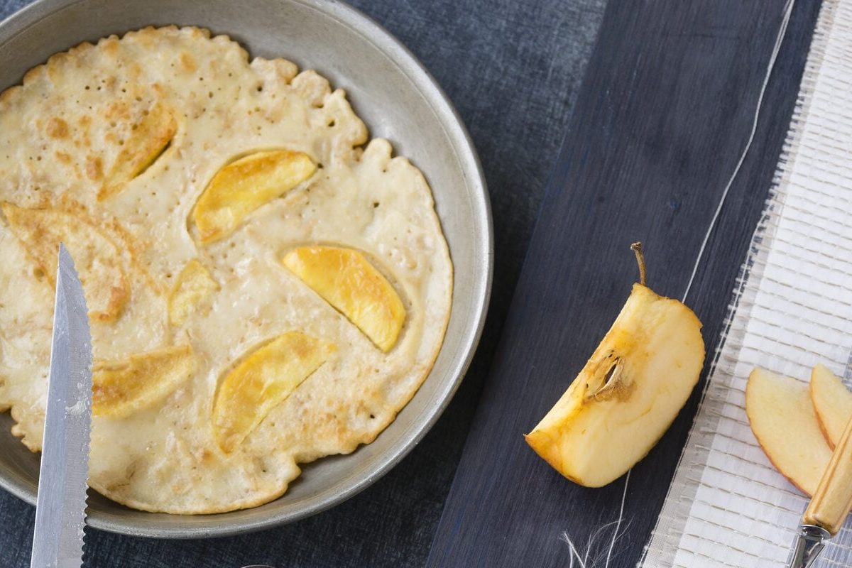 Schnelle Pfannkuchen mit Apfel in Pfanne, daneben Apfel