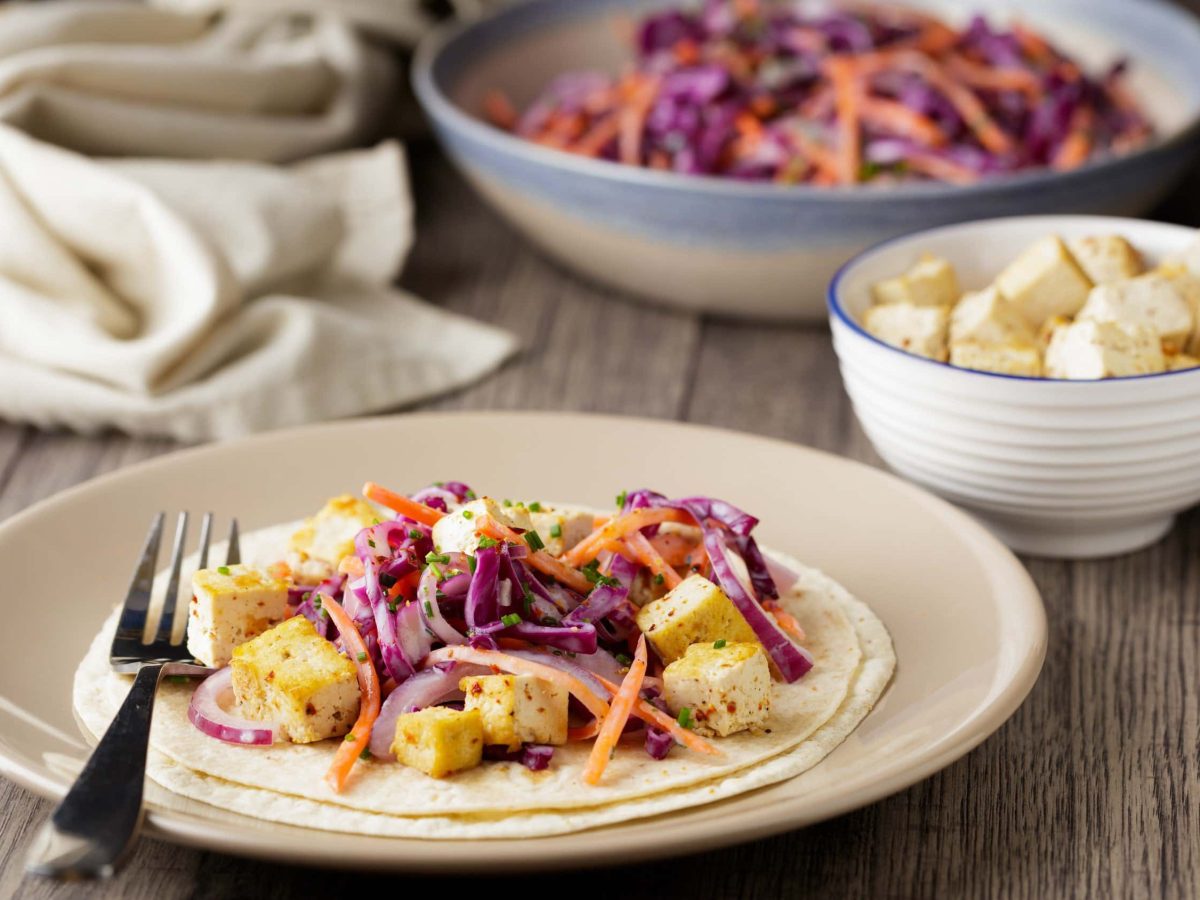 Tofu-Wrap mit Krautsalat auf einem hellen Teller, serviert mit frittierten Tofuwürfeln und Krautsalat in verschiedenen Schalen auf einem Holztisch