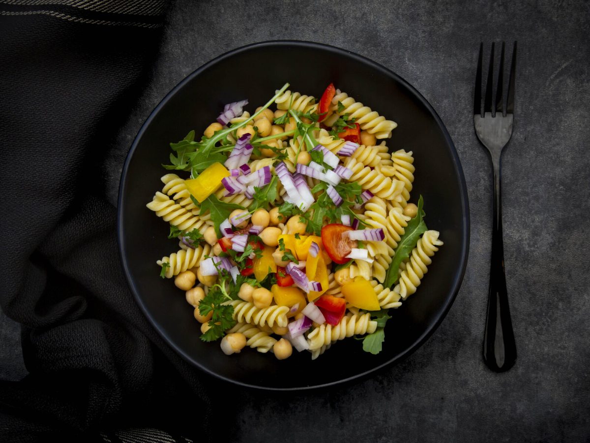 Rucola-Nudel-Salat mit Kichererbsen in schwarzer Schüssel, daneben Gabel