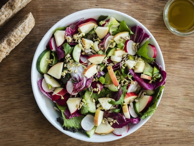 Bunter Apfelsalat mit Radicchio, Gurke, Roma-Salat, Sprossen und leichter Salat-Sauce, serviert in einer großen Schale auf einem Holztisch mit Brot.