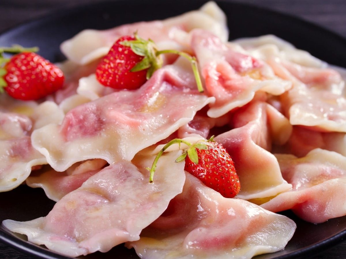 Fruchtig gefüllte Pierogi mit Erdbeerfüllung, ausgekocht und serviert auf einem dunklen Teller, garniert mit frischen Erdbeeren.