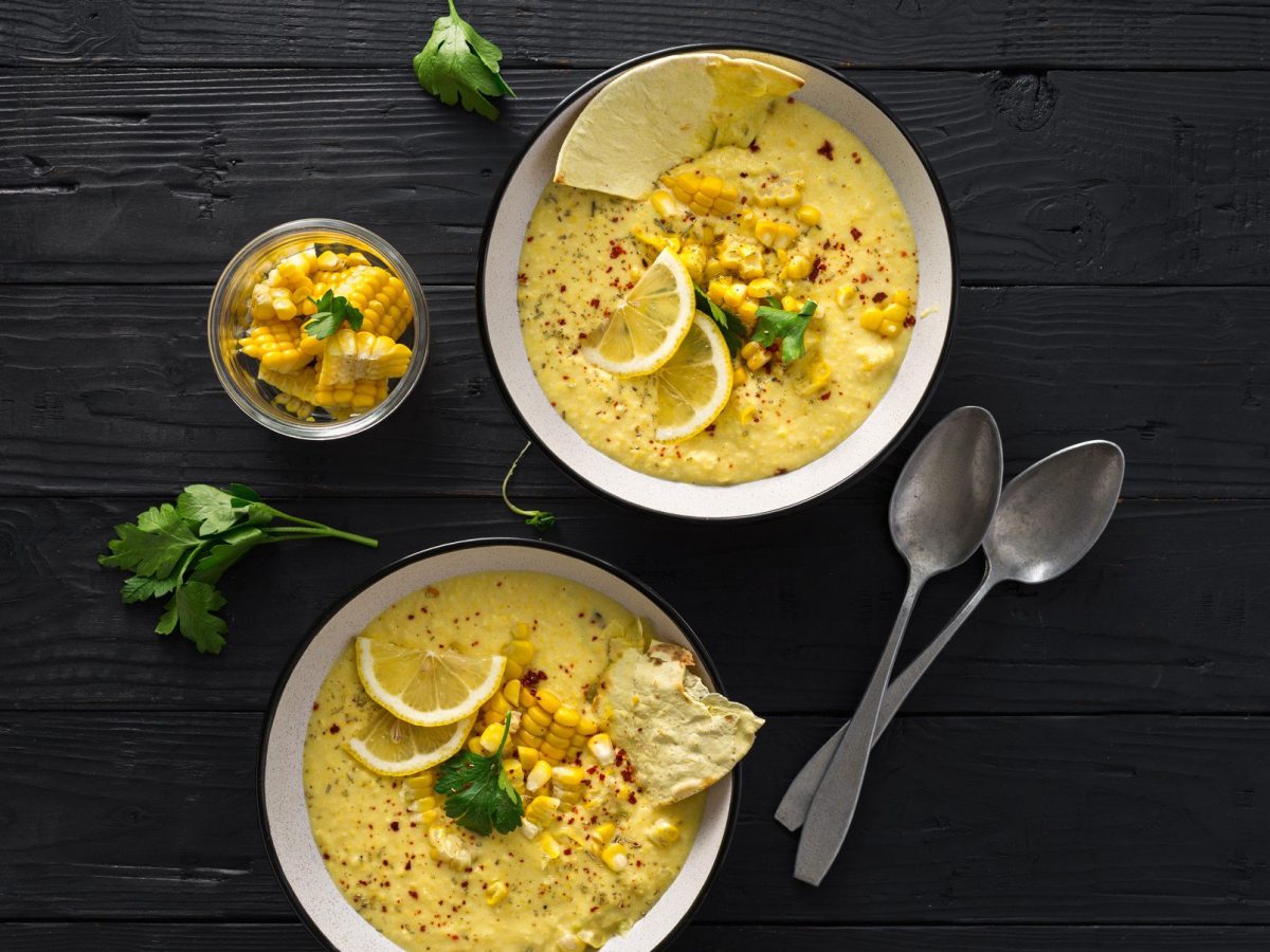 Zwei Teller mit cremiger Maissuppe mexikanischer Art gespickt mit Zitronenscheiben und Korianderblättern auf schwarzem Hintergrund