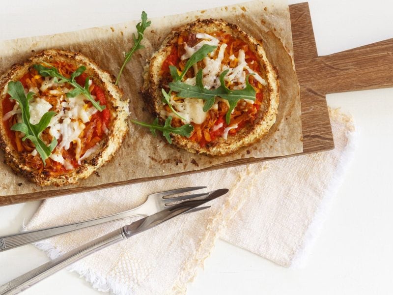 Protein-Pizza aus Blumenkohl auf Holzbrett garniert mit Rucola