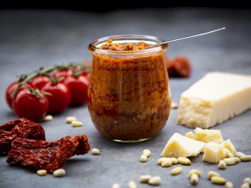 Glas mit Pesto auf dunklem Hintergrund mit rotem Parmesan, Kirschtomaten und Pinienkernen