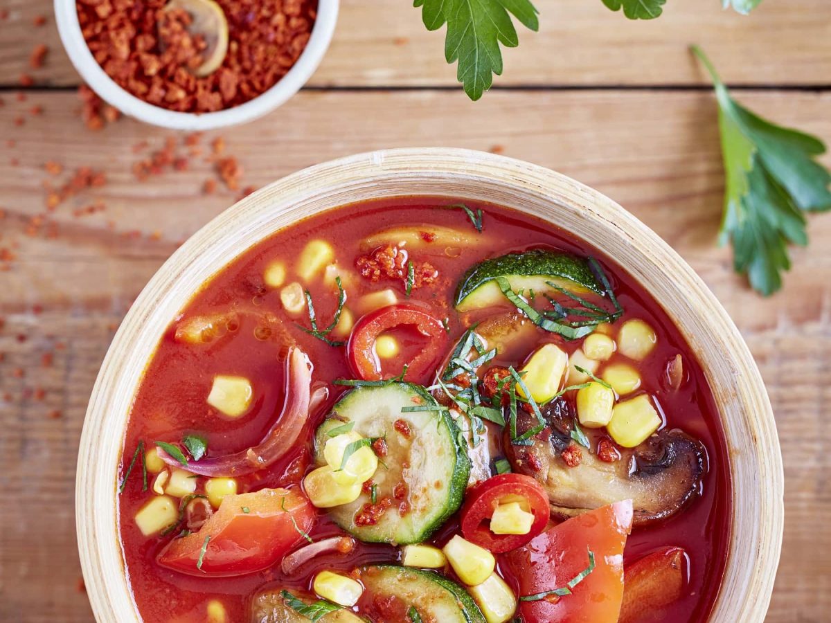 pikante Gemüsesuppe mit Chili und Mais in Schüssel, daneben Chilli und Petersilie