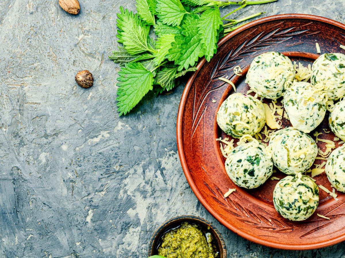 Würzige Malfatti, bestehend aus Spinat, Käse und Mehl, serviert in einer braunen Tonschale mit geriebenem Käse und frischer Brennnessel und Pesto