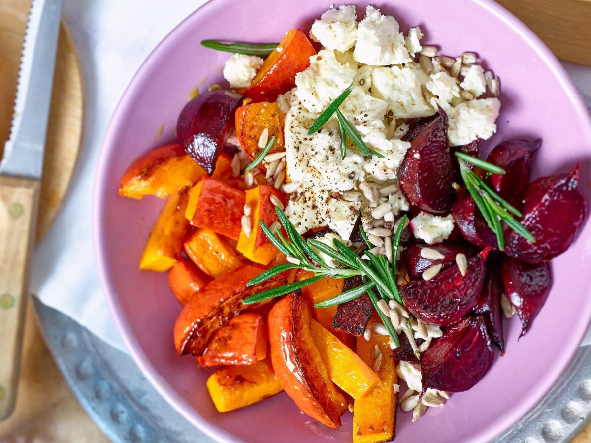 Herbstliche Buddha-Bowl mit Feta-Topping in pinker Schüssel, daneben Messer