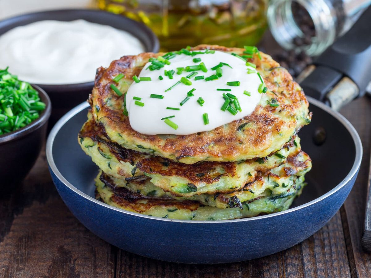 Zucchini-Karotten-Puffer mit selbst gemachtem Quark-Dip in Teller, dahinter Schüssel mit Dip