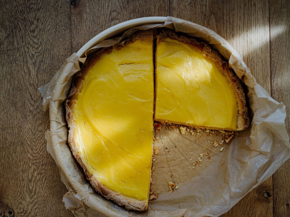 angeschnittene Tarte au Citron in Backpapier und Backform auf holzigem Untergrund