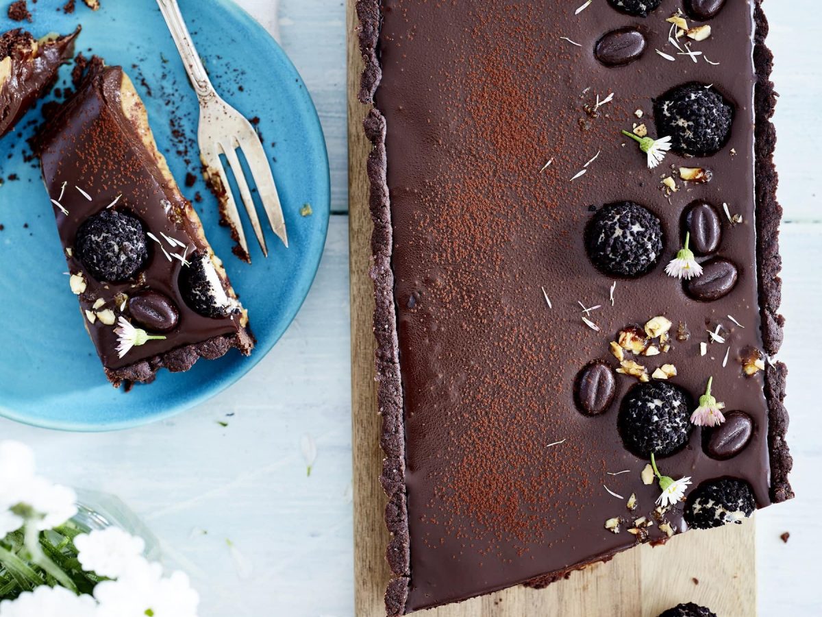 Tarte au Chocolat mit Erdnuss und Espresso auf Holzbrett, ein Stück auf blauem Teller