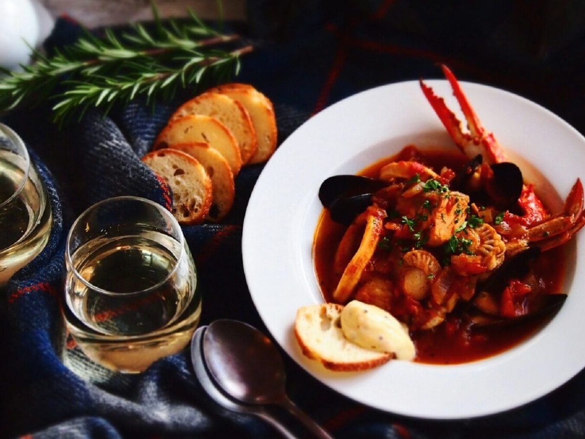 Weißer Teller mit Bouillabaisse, zwei Gläsern Weißwein und Weißbrot