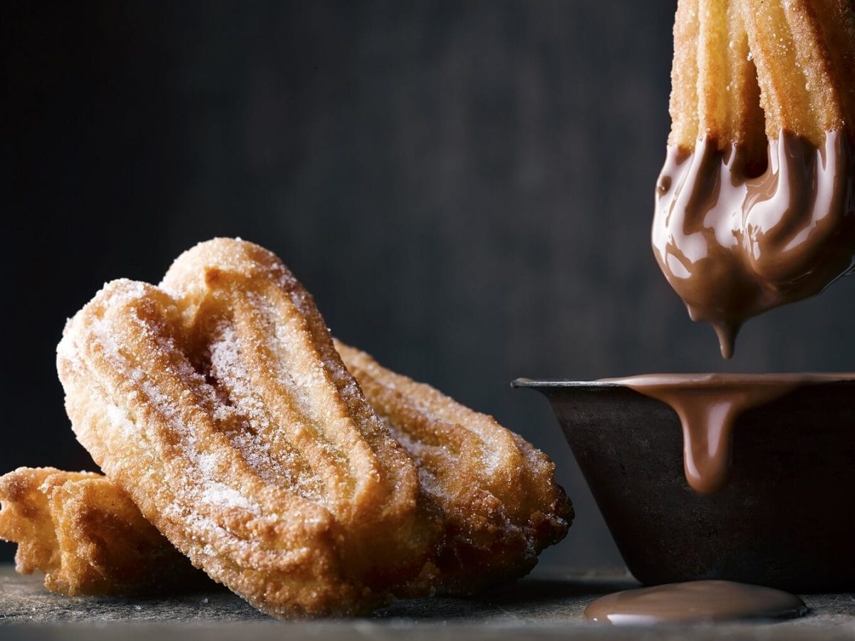 Churros mit Schokoladensauce vor dunklem Hintergrund