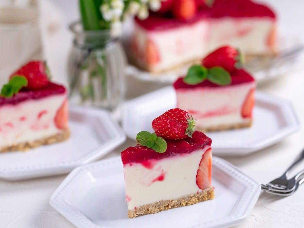 Beeren-Quark-Torte auf Tellern mit Besteck auf einem gedeckten Tisch mit Blumen in einer Vase