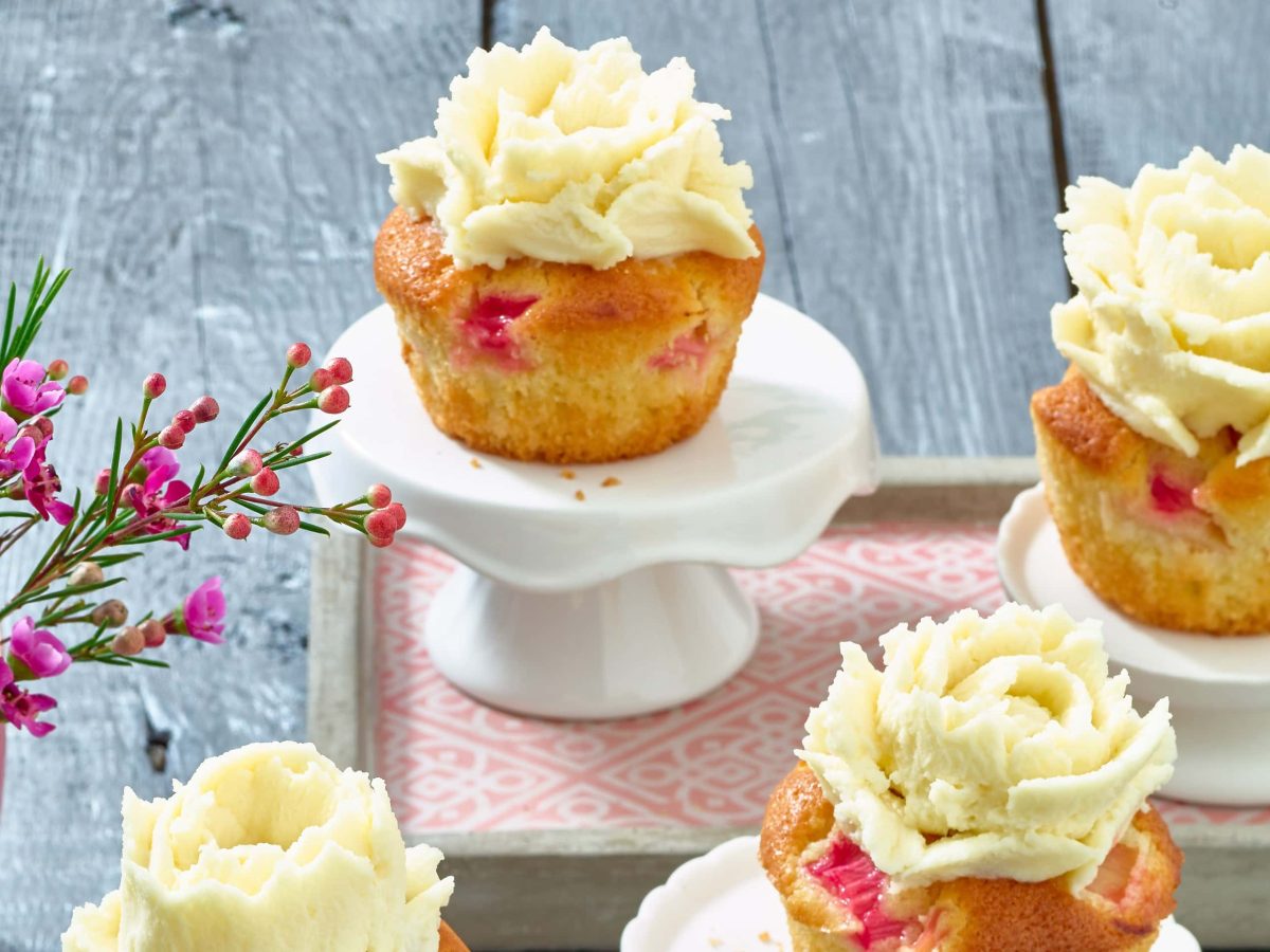 Rhabarber-Cupcakes mit Marzipan stehen auf kleinen Etageren neben einer Vase mit Blumen