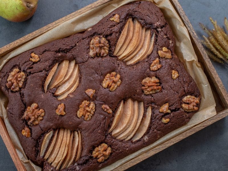 Schoko-Birnenkuchen mit Walnüssen in Backform, daneben getrocknete Gräser